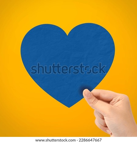 Hand holding paper heart on yellow background