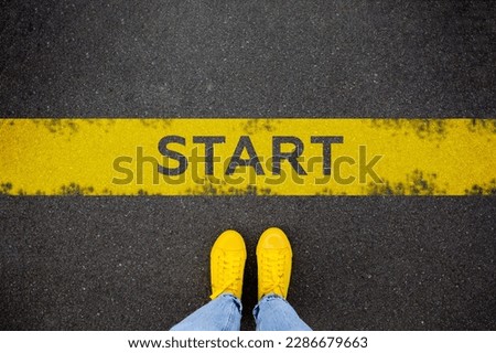 Female feet in yellow sneakers standing on street background with word new start written. Yellow race line beginning idea concept. Top view. Businessman of starting Royalty-Free Stock Photo #2286679663