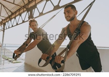 Cool strong young sporty athletic toned fit sportsman man in sport clothes warm up suspended training work out with TRX trainer at sunrise sun dawn over sea beach seaside outdoor in summer day morning Royalty-Free Stock Photo #2286709291