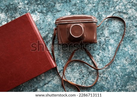 A vintage old camera in a brown leather case and stylish brown photo books lie on a textured blue stone tabletop. Image for your creative design or illustrations.