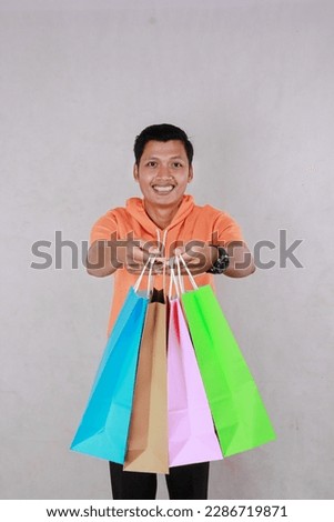 portrait of mature Asian man wearing orange t-shirt looking at paper bag, groceries with smiling expression isolated on white background