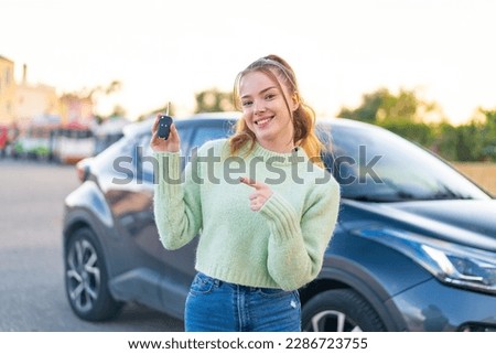 Young pretty girl holding car keys at outdoors and pointing it