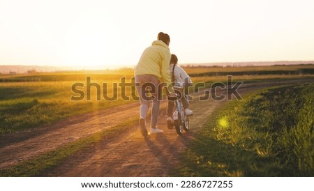 mother rides child bicycle sunset. happy family park. Mom teaches her daughter ride bike. concept happy family summer park. fun vacation. teamwork. mother runs green grass rolling child bicycle. Royalty-Free Stock Photo #2286727255