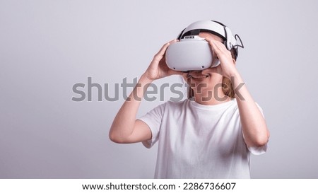 Surprised teen woman student use vr glasses and looks at empty space with gray background. Virtual gadgets for entertainment, work, free time and study. Virtual reality metaverse technology concept.