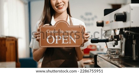 Young female entrepreneur hanging a welcome sign in front of a coffee shop. Beautiful waitress or hostess holding a tablet preparing  in cafe