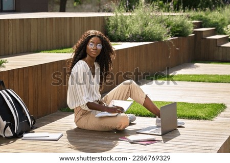 African girl, pretty black female university student taking notes elearning with laptop computer studying outdoor on sunny day in campus writing thinking, remote learning, online education concept.