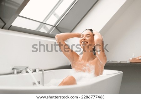 Young Woman Enjoying Taking Bath And Washing Head Applying Shampoo On Hair Posing With Eyes Closed In Modern Bathroom At Home. Haircare Cosmetics Concept. Selective Focus