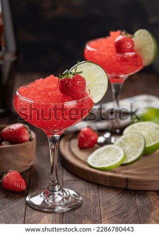 Frozen strawberry daiquiri garnished with strawberries and lime slice on a rustic wooden background