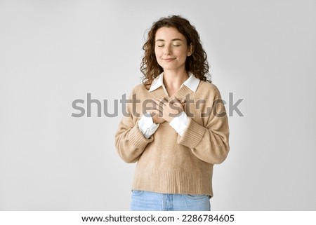 Happy pleased pretty young woman holding hands on chest feeling gratitude, mental balance, expressing thanking, kindness and love in heart standing isolated at white background. Royalty-Free Stock Photo #2286784605
