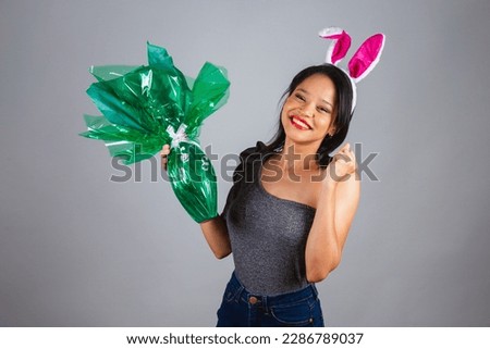 Brazilian woman, northeastern, wearing bunny ears, photo for Easter. holding green easter egg, chocolate shaped like an egg.
