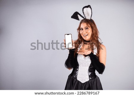 Beautiful Brazilian woman, with rabbit clothes, Easter. holding smartphone, showing white screen for advertisement, ads, mobile apps.