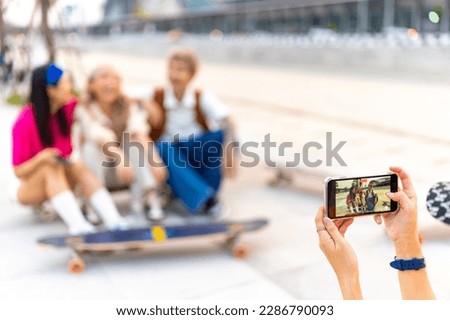 Group of Stylish youth people Asian man and woman friends have fun urban outdoor lifestyle using mobile phone taking picture together during skating on longboard skate in the city on summer vacation.