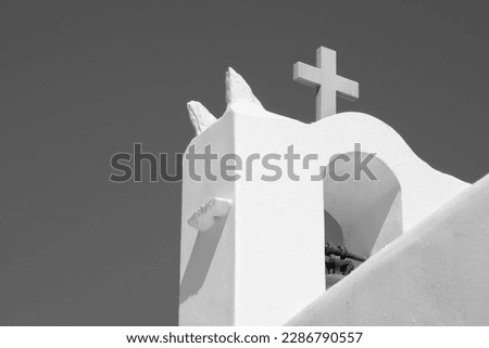 A cross on the top of an orthodox whitewashed church in Ios Greece and a blue sky in the background in Ios Greece in black and white
