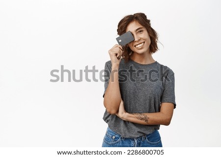 Portrait of beautiful young woman showing credit card, recommending bank, contactless shopping or discounts in store, time to shop, standing over white background.