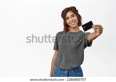 Portrait of beautiful young woman showing credit card, recommending bank, contactless shopping or discounts in store, time to shop, standing over white background.