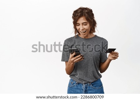 Online shopping. Smiling young woman using mobile phone and credit card to pay, make purchase, order or register in web store, standing over white background.