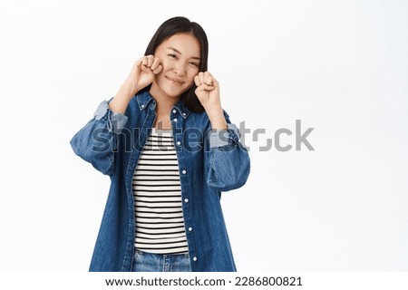 Cute asian girl makes kawaii paws gesture near face, posing silly against white studio background.