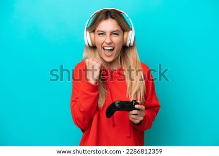 Young Uruguayan woman playing with a video game controller isolated on blue celebrating a victory in winner position