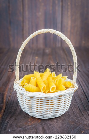 Raw pasta on basket on  wooden background - process old dark style picture