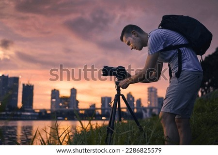 Concentrated photographer with camera on tripod during taking photo of urban skyline. Modern city during beautiful sunset, Singapore.
 Royalty-Free Stock Photo #2286825579