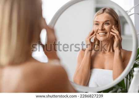 Anti-Aging Cosmetics. Beautiful Middle Aged Woman Applying Eye Cream While Standing Near Mirror At Home, Attractive Mature Lady Touching Her Face, Enjoying Daily Beauty Routine, Selective Focus Royalty-Free Stock Photo #2286827239