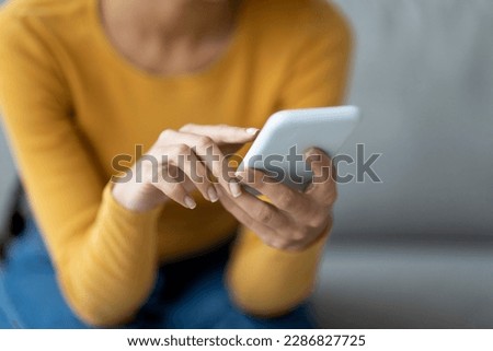 Unrecognizable Lady Using Modern Smartphone While Sitting On Couch At Home, Closeup Shot Of Female Hands Holding Cellphone, Young Woman Browsing App On Mobile Phone Or Shopping Online, Cropped Royalty-Free Stock Photo #2286827725