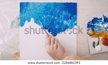 Art studio. Creative process. Abstract artwork. Unrecognizable woman painting with spatula and blue paint on white canvas.