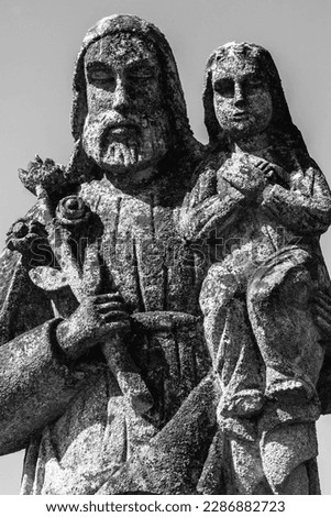 Saint Joseph with little Jesus Christ. Very ancient stone statue. White and black vertical image.
