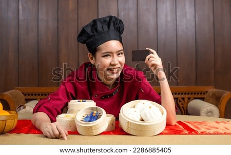 Beautiful Asian female chef wearing uniform, holding, presenting credit card for payment, showing food, smiling with happiness. Restaurant Concept