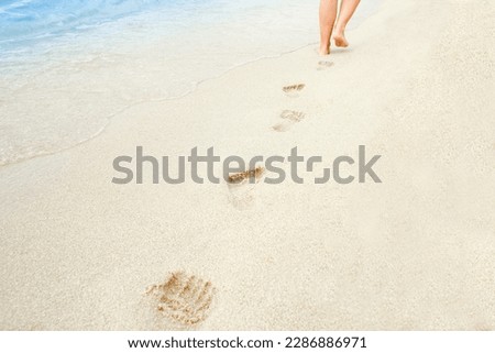 Beach travel - woman relaxing walking on a sandy beach leaving footprints in the sand. Close up detail of female feet on golden sand at a beach in Greece. Background.
