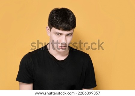 Offended aggrieved teenage boy looks from under forehead, the boy is sad and very worried about studying in college, he is offended at teachers. Sad not cheerful young guy on yellow background Royalty-Free Stock Photo #2286899357