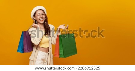 Smiling pretty Asian teen woman carrying shopping bags on yellow color studio background. happy shopping summer sale. copy space
