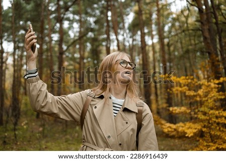 Woman hand is holding a phone with sign no service above his head against the background of trees in a pine forest. Concept of no service, wifi, internet in the forest or a place far from the city