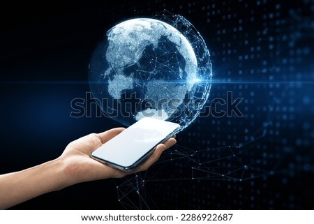 Close up of female hand holding cellphone with glowing blue polygonal globe hologram on dark background