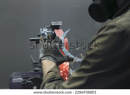 The process of sharpening a metal sickle on a grinder. The horizontal photo shows the hands of the master sharpening, bright red sparks fly from the sickle