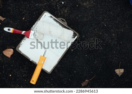 Unrecognizable young man uses a paint roller to apply special acrylic paint for road marking on asphalt.