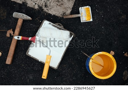 Unrecognizable young man uses a paint roller to apply special acrylic paint for road marking on asphalt.
