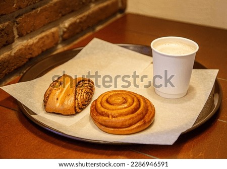A poppy seed and cinnamon bun and a cup of coffee on a vintage tray in a bakery. Continental breakfast at the bakery. Coffee in a paper cup and sweet rolls.