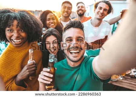 Multiethnic group of friends hanging out on a dinner rooftop party - Multiracial young people having fun enjoying together summertime days - Life style concept with guys and girls laughing outside 