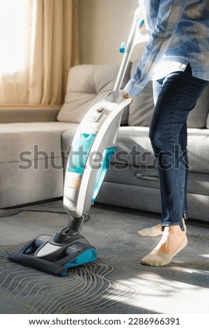 Vacuum cleaner is used to clean the carpet in the room. Housework with a new handheld vacuum cleaner. House cleaning, care and technology concept. A young woman is cleaning the living room. Royalty-Free Stock Photo #2286966391