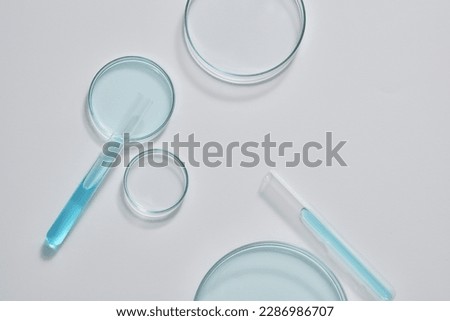 Minimal scene with some glass petri dishes decorated with test tubes filled with blue fluid on white background. Empty area for product display, copy space Royalty-Free Stock Photo #2286986707