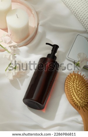 Candles placed on a pink marble dish, unlabeled pump bottle dispenser arranged with flowers, hand mirror and wooden brush. Branding shampoo mockup