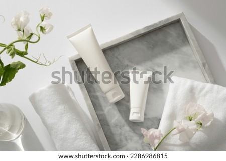 A gray marble tray with towel, flower branch and two white tube displayed on, white flower branches inside a glass transparent pot. Gentle skin care concept Royalty-Free Stock Photo #2286986815