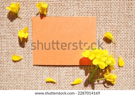 Spring-like orange message space mockup with scattered rape blossoms against a background of wheat-colored jute cloth
