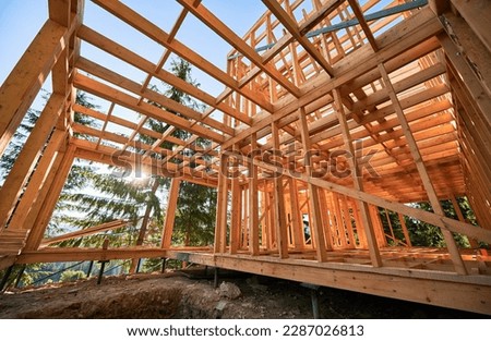Housing wooden-frame house built near woodland area. Start of novel construction of comfortable cottage on edge of the forest. Concept of contemporary ecological construction and modern architecture. Royalty-Free Stock Photo #2287026813