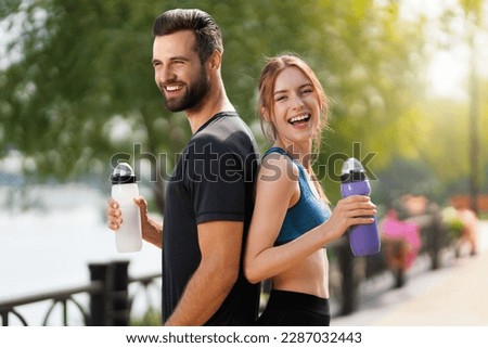 Portrait image of happy smiling, excited couple holding plastic water bottles, woman with man or bearded coach trainer, after successful training, outdoors. Fitness, sport, workout concept. Royalty-Free Stock Photo #2287032443