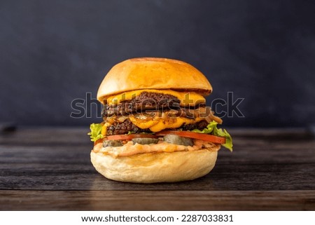 Isolated double cheese burger with tomate, lettuce, pickles, sweet onions and sauce in a dark background. Hamburger with two patties and salad in wooden table