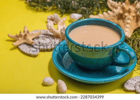 A cup of coffee in a marine style. Starfish, sea shells, palm leaves. Hard light, dark shadow, bright yellow background, close up