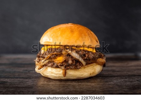 Isolated double cheese smash burger with sweet onions and sauce in a dark background. Hamburger with two patties and salad in wooden table Royalty-Free Stock Photo #2287034603