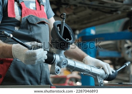 The steering rack is in the hands of an auto mechanic. A component of the hydraulic power steering of the car. Monitoring of the technical condition of the new spare part before installation. Royalty-Free Stock Photo #2287046893
